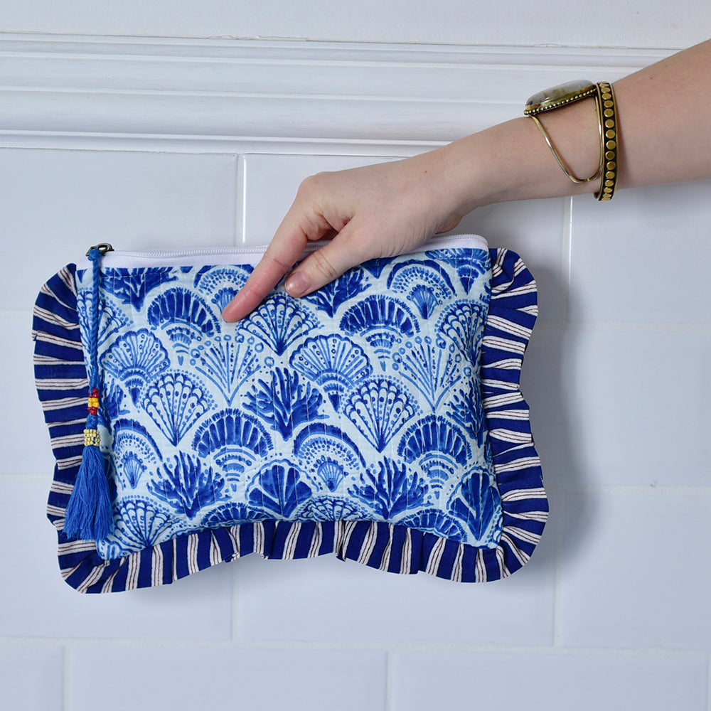 Blue and White Wide Stripe Seashell makeup bag held by a hand against a white tiled wall.