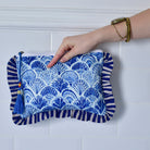Blue and White Wide Stripe Seashell makeup bag held by a hand against a white tiled wall.