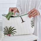 Palm tree print wash bag on white background with green pom pom trim.