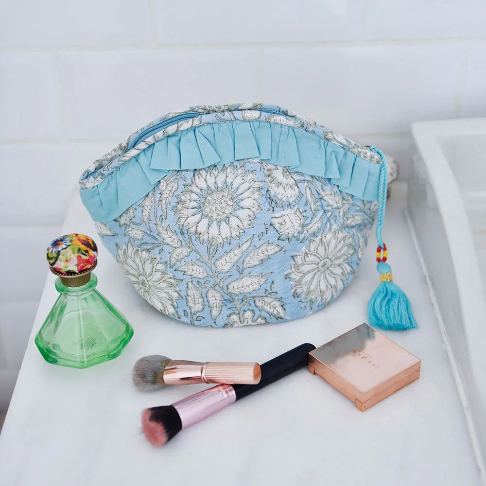 Cornflower blue wash bag with cosmetic items on a white surface