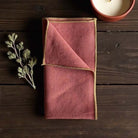 Rust coloured napkin with gold piped edges.