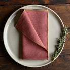 Rust coloured napkin with gold piped edges.