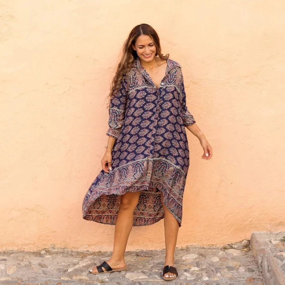 Woman wearing a patterned dress standing against a beige wall.