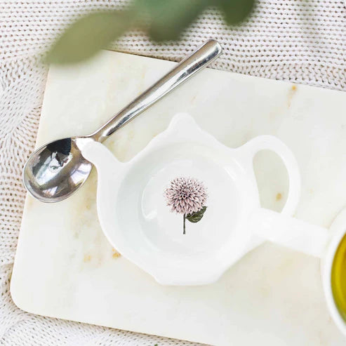 White ceramic spoon rest with a pink flower design on a marble surface.