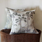 Decorative pillows with Tropical Fern and Tropical Palm tree designs on a wicker basket against a neutral wall.