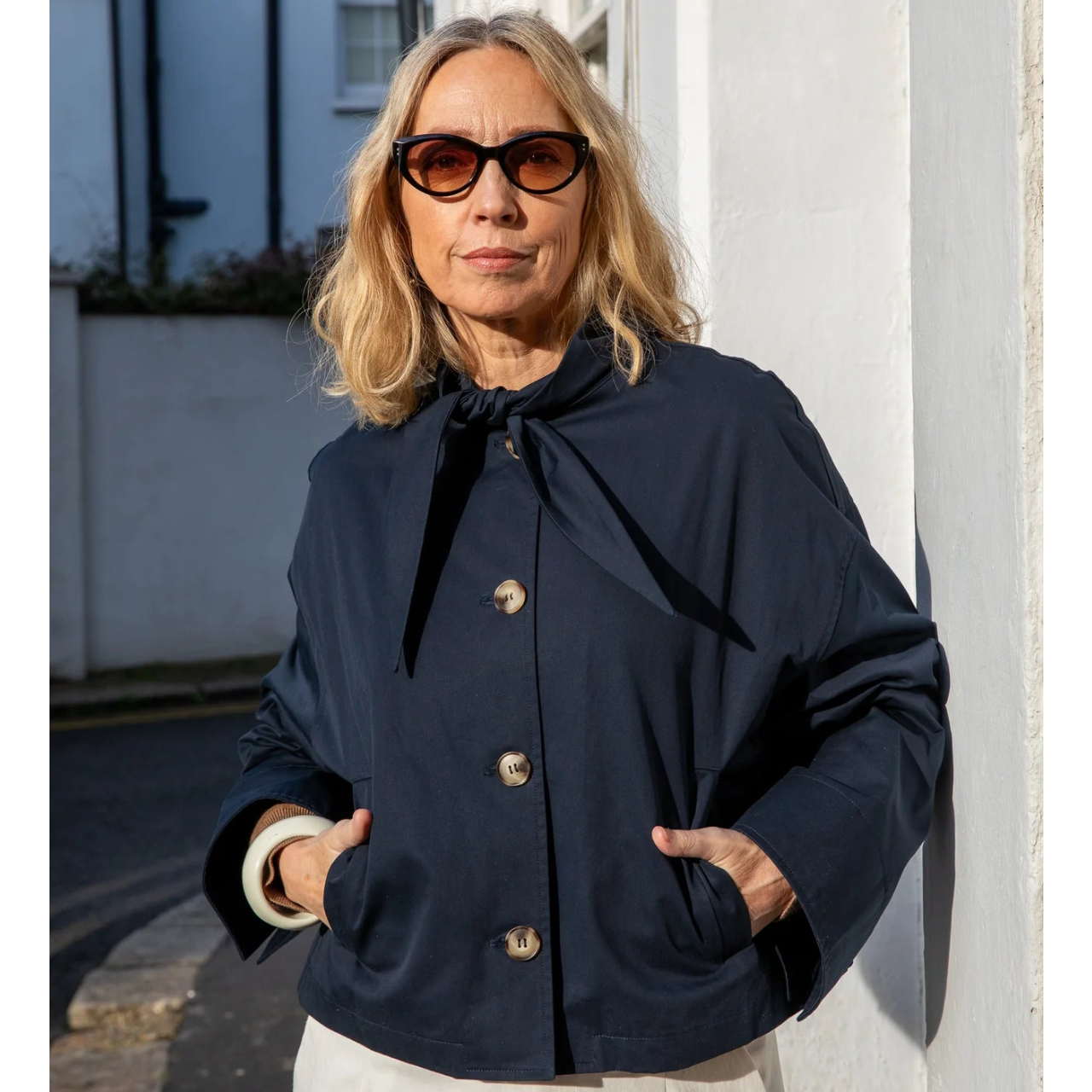 Woman wearing a navy blue coat with a black ribbon, standing outdoors.