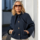 Woman wearing a navy blue coat with a black ribbon, standing outdoors.