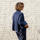Person wearing a navy blue jumper standing against a white brick wall