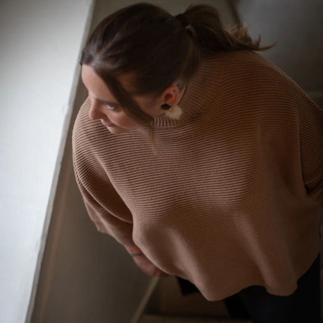 Person wearing a beige sweater sitting on a staircase.