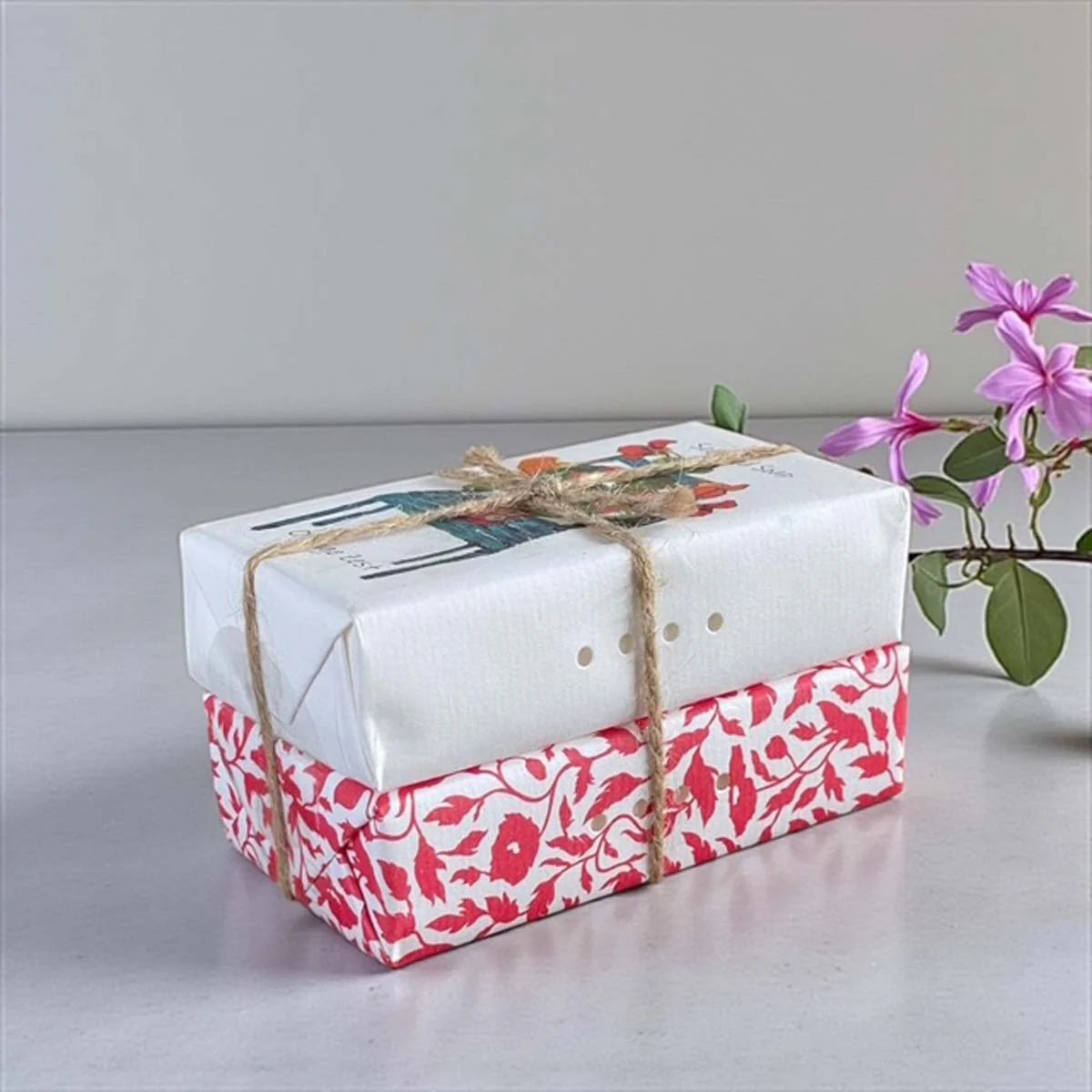 Two bars of soap wrapped in decorative paper and tied with jute string.