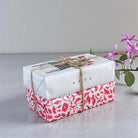 Two bars of soap wrapped in decorative paper and tied with jute string.