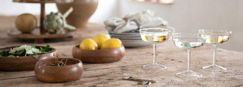 Wooden bowls on rustic table with lemons, bowls, and glasses in a bright room.