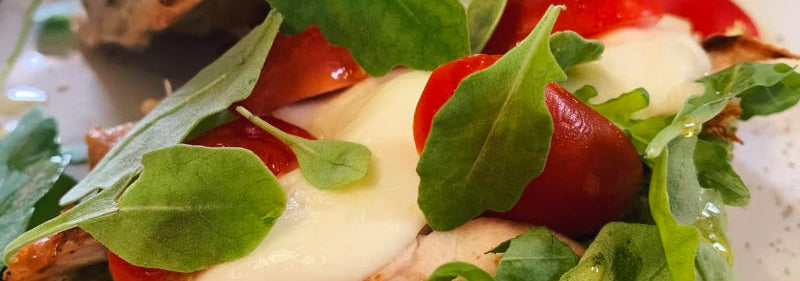 Sandwich with chicken, tomatoes, and greens on a plate