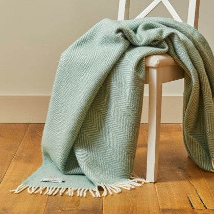 Green blanket draped over a white chair on a wooden floor.