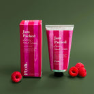 Jam Packed Luxury Hand Cream with packaging and raspberries on a green background