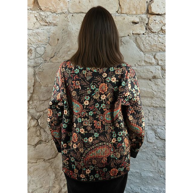 Person wearing a patterned jacket standing against a stone wall