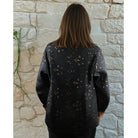 Person wearing a dark sweater with subtle patterns against a stone wall.