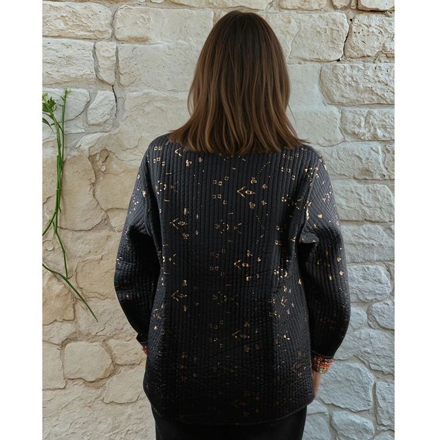 Person wearing a dark sweater with subtle patterns against a stone wall.