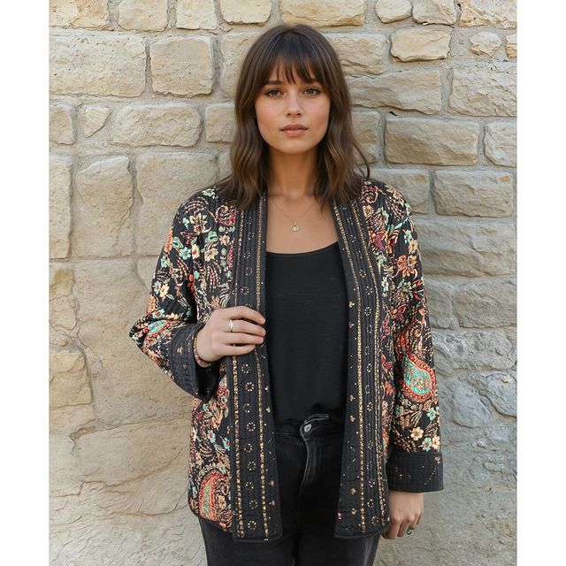 Woman wearing a patterned jacket against a stone wall