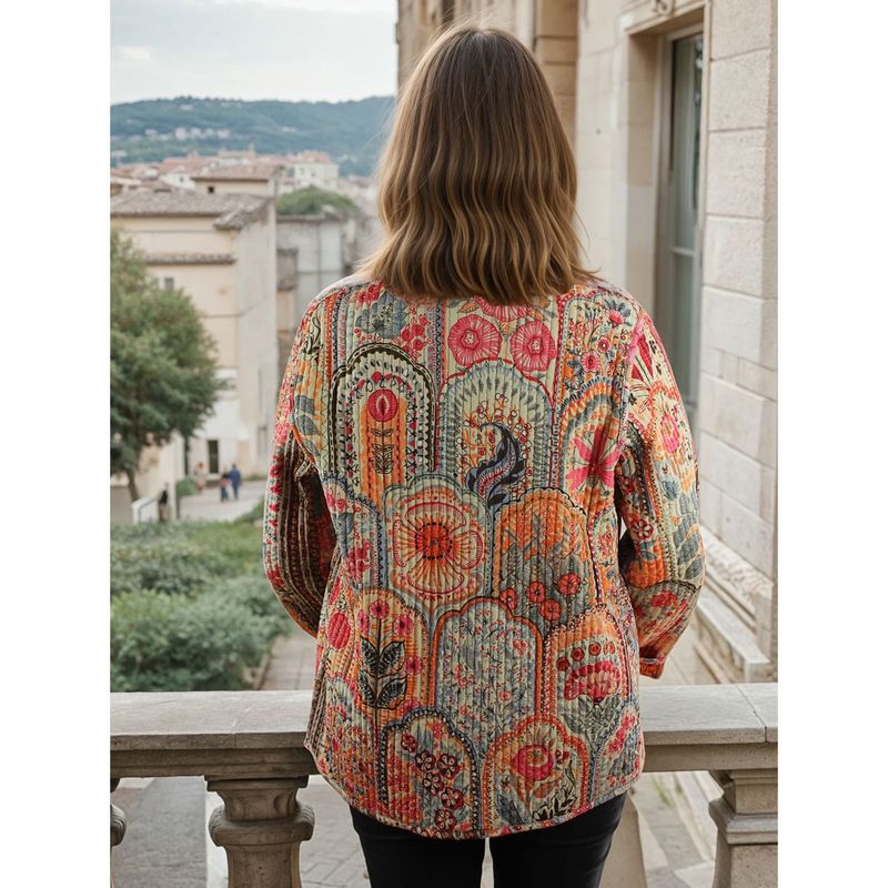 Woman wearing a colorful patterned jacket standing on a balcony with a scenic view.