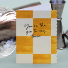 Greeting card with checkered design and text 'You're the gin to my tonic' next to cocktail shakers on a light blue background