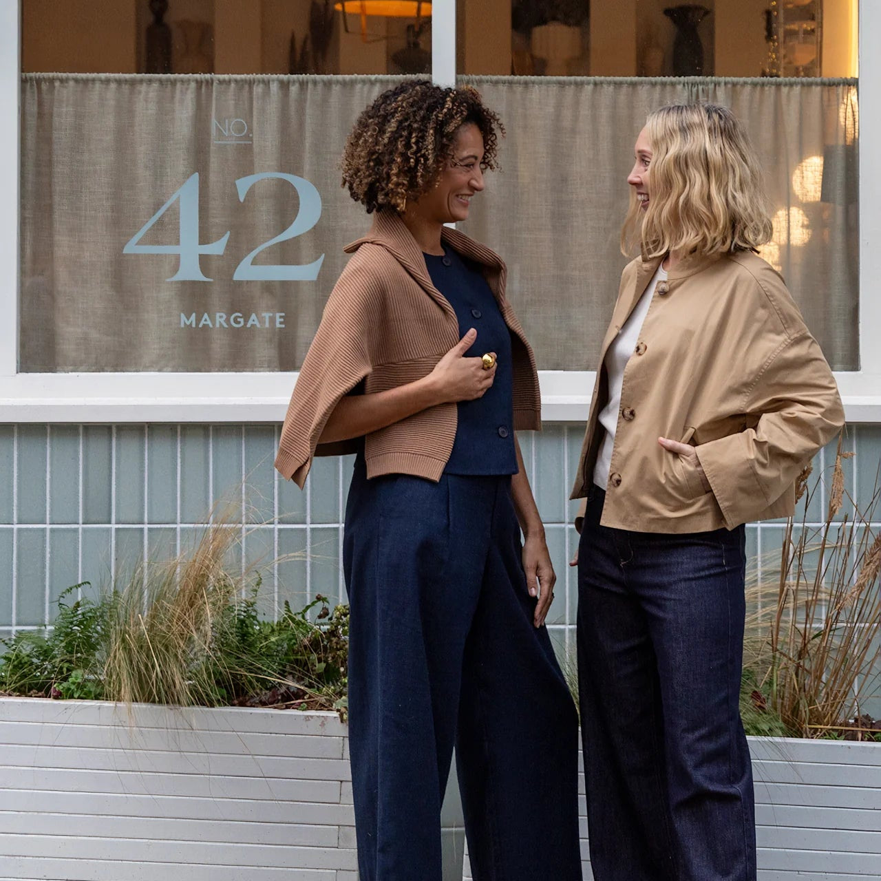 Two women standing outside a building dark tan jumper