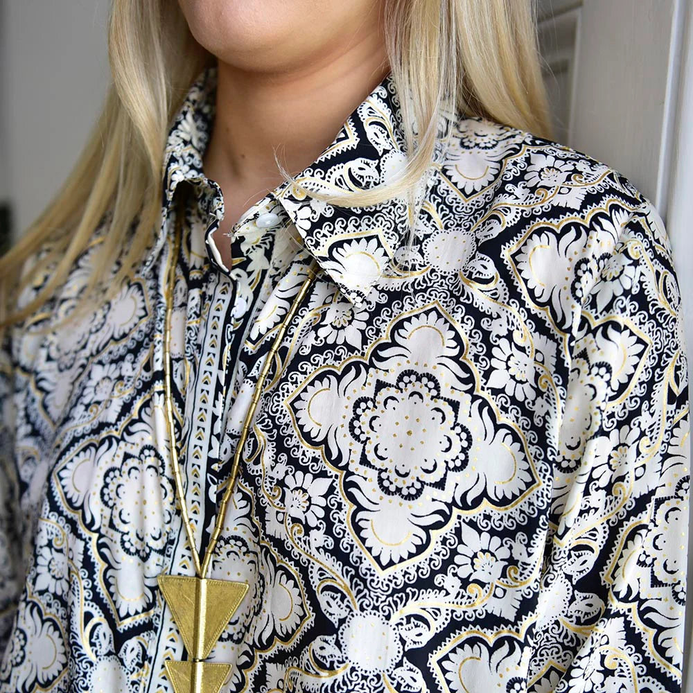 Person wearing a black and white patterned shirt with a gold necklace.